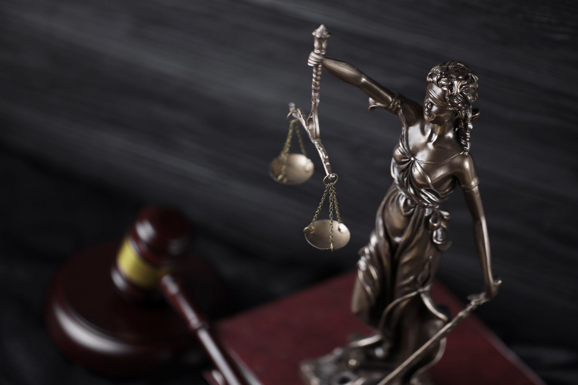 Statue of Lady Justice with scales, a gavel, and a book on a dark background.