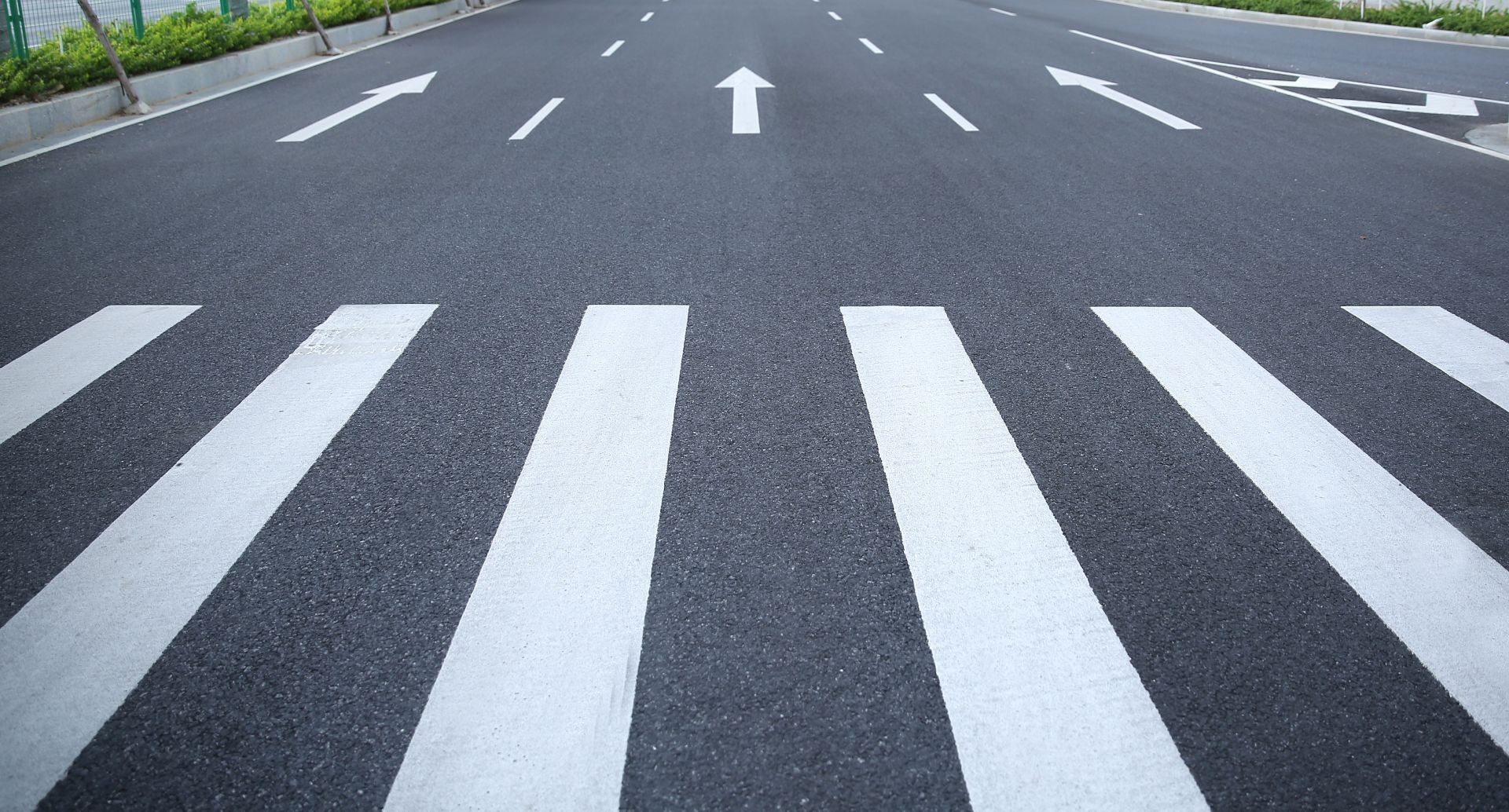 Crosswalk on asphalt road with lane markings and directional arrows.