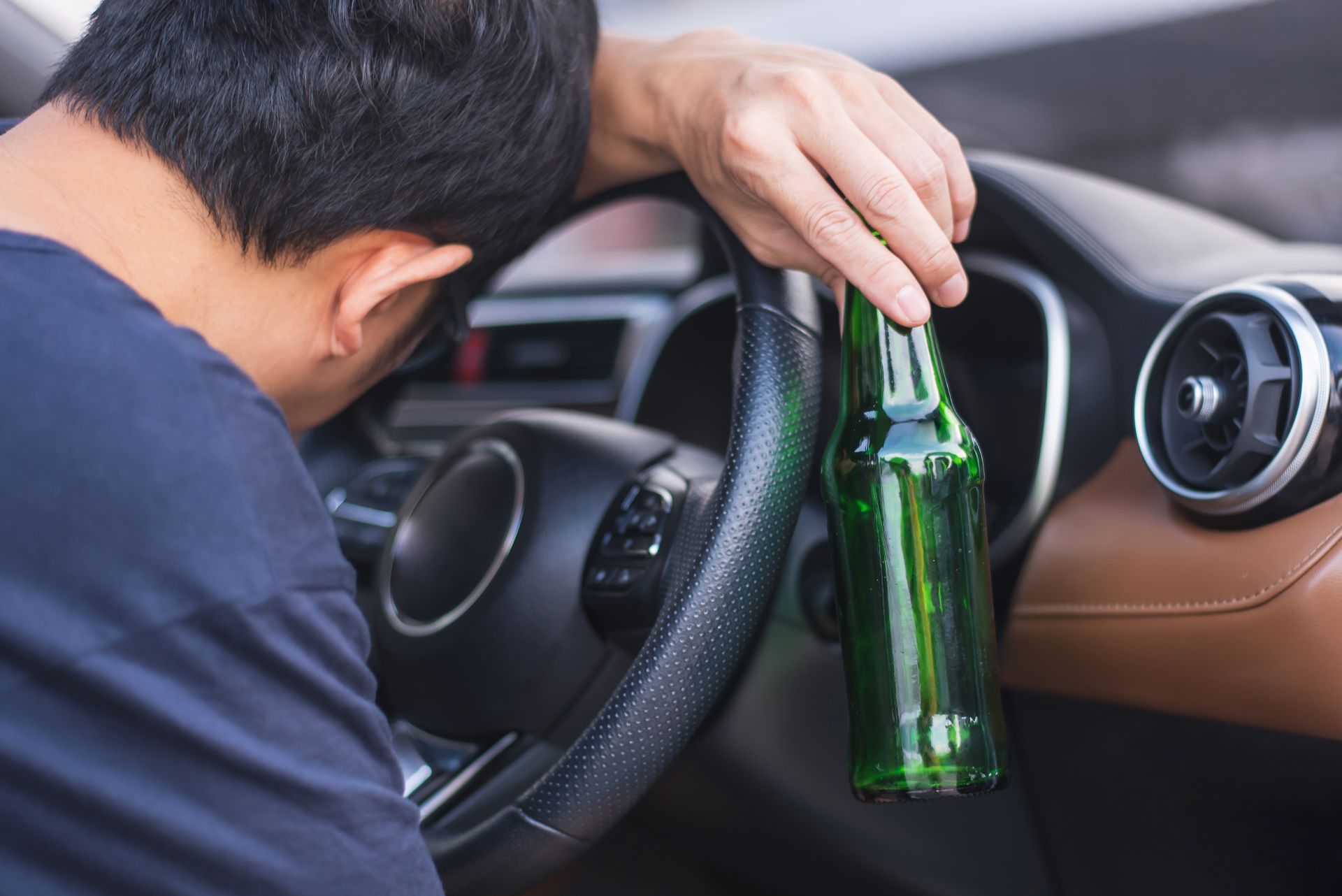 Man slumped over steering wheel, holding a beer bottle, inside a car.