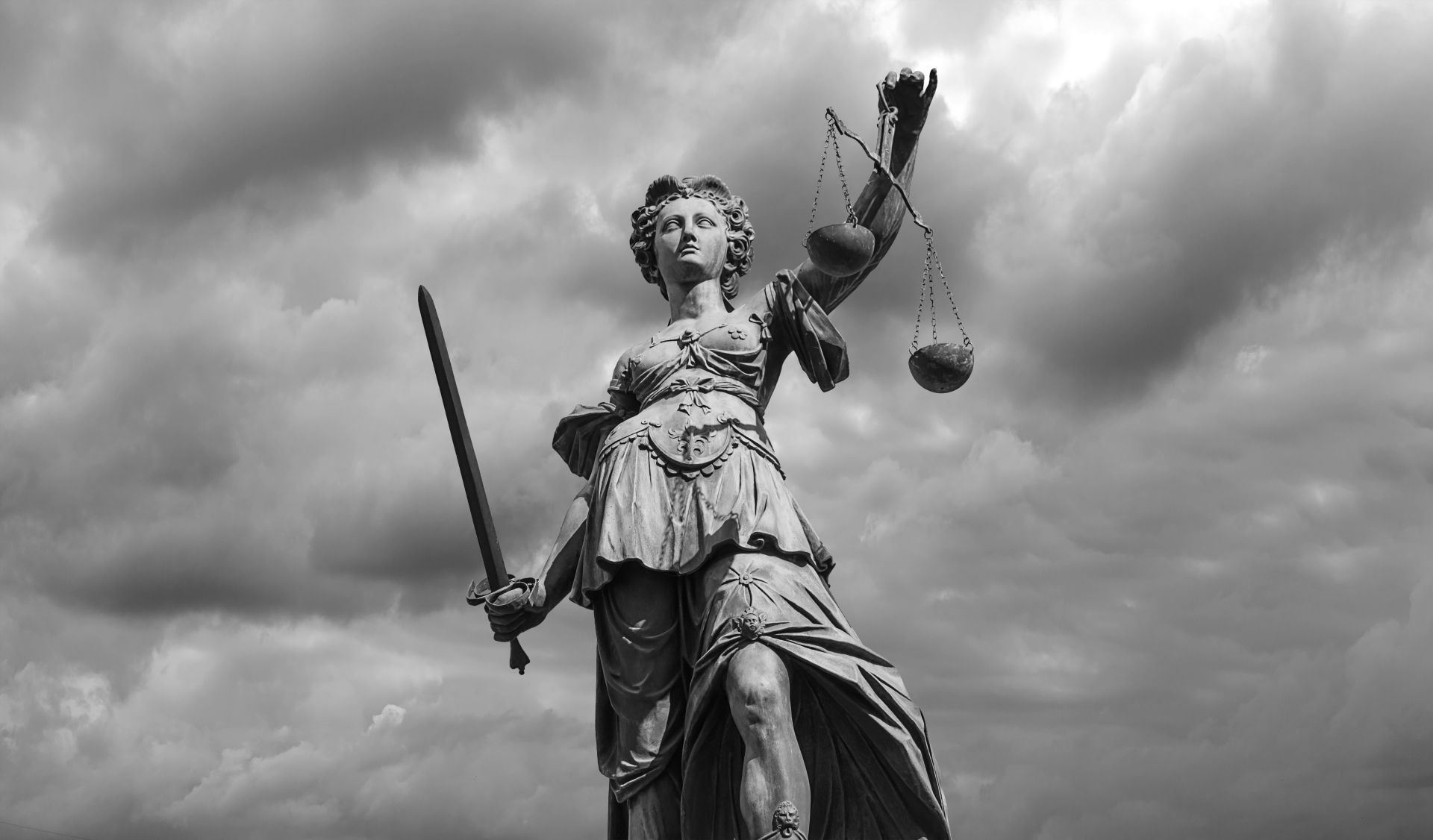 Statue of Lady Justice with scales and sword, set against a cloudy sky.