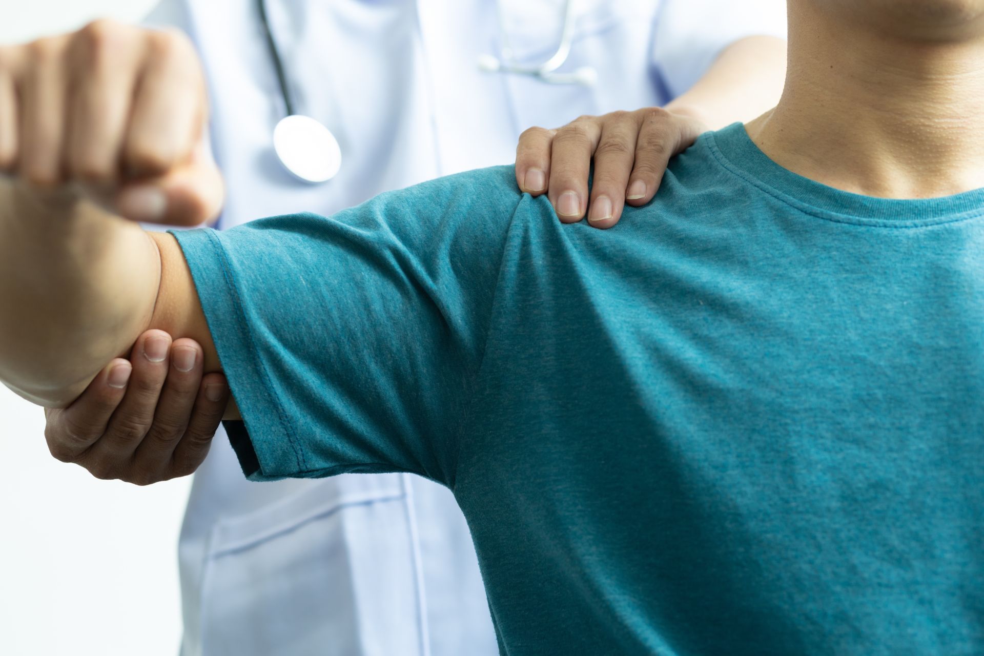 A medical professional examines a patient's shoulder. The patient wears a blue shirt.