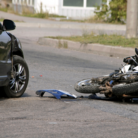 Car and motorcycle accident scene on a road; damaged vehicles and debris visible.