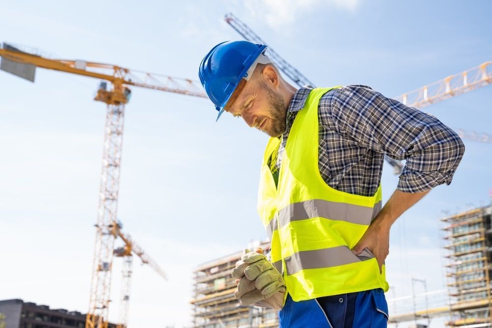 Construction worker holding his back in pain, on a building site.