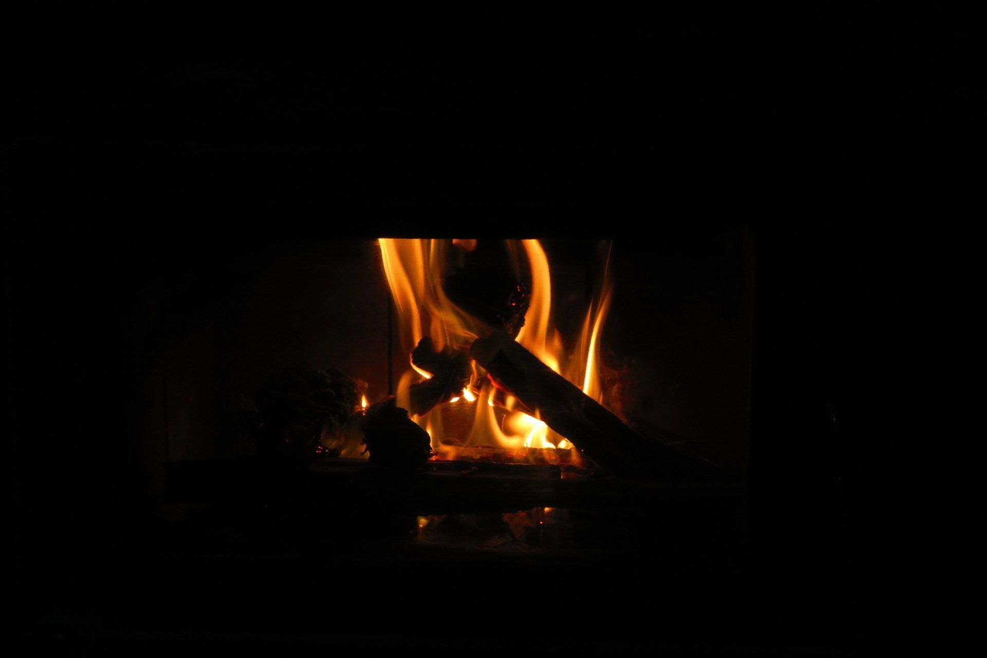 Cozy living room with a lit fireplace, stone hearth, wooden beams, windows, and leather chairs.