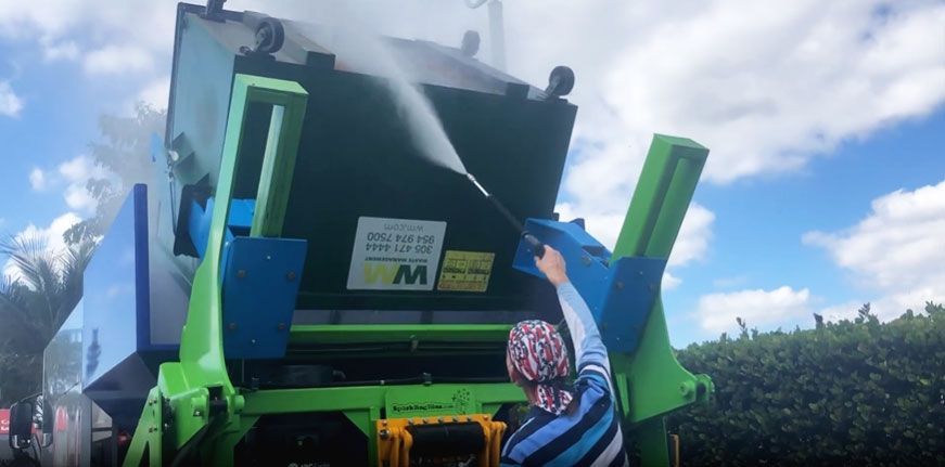 A man is spraying a green trash can with a spray bottle.