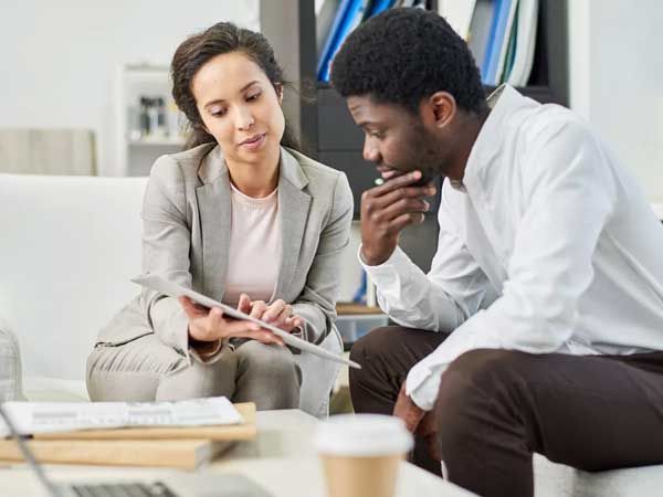 A man and a woman are sitting on a couch looking at a tablet.