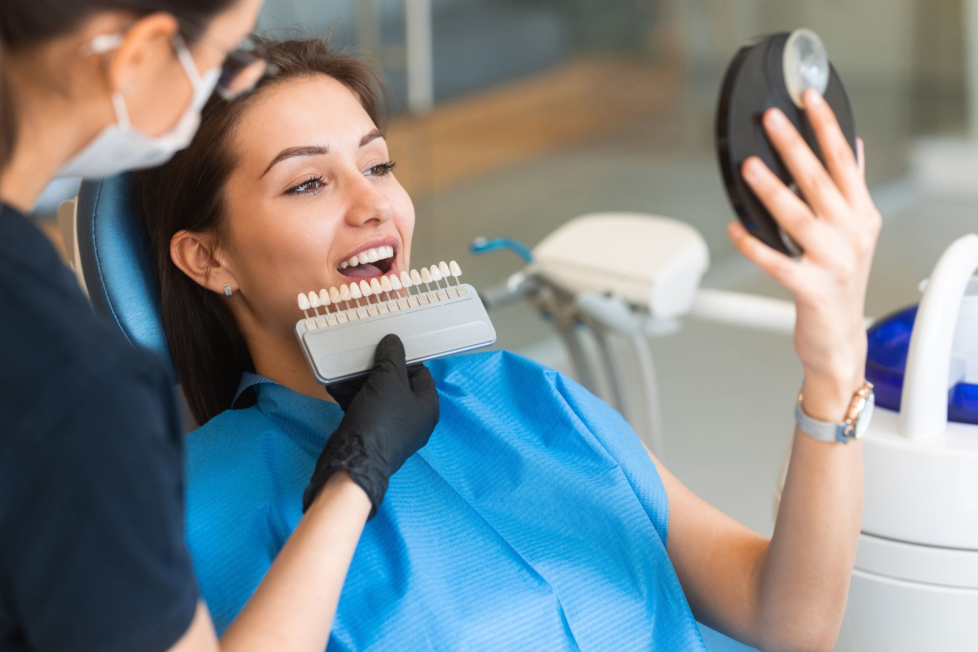 A dentist uses a tooth shade guide to match color for veneers during a cosmetic dental consultation. A dentist uses a tooth shade guide to match color for veneers during a cosmetic dental consultation.