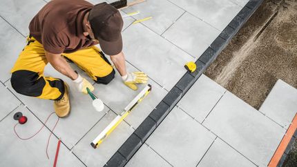 A man is kneeling down on the ground while working on a patio.