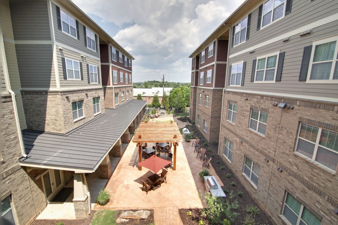 Communal courtyard between multi-story apartment buildings with patio tables and a pergola.
