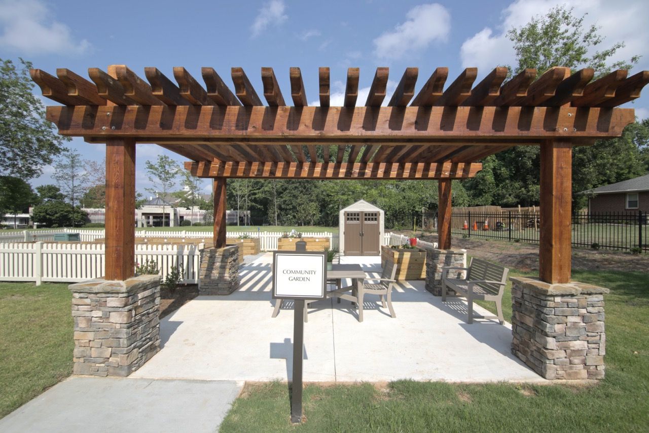 Wooden pergola over a paved seating area with a sign reading 'Community Garden'.