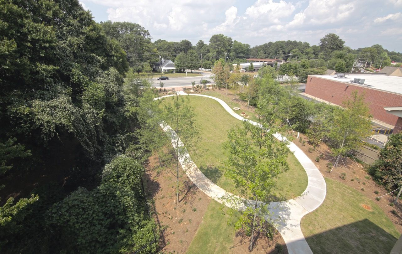 Aerial view of a curved concrete walkway winding through a landscaped courtyard with trees at an apartment complex.
