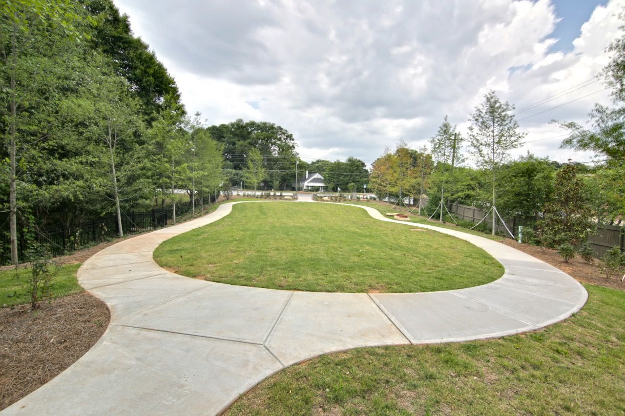 Curved concrete walkway around a circular grassy lawn in a landscaped outdoor community area.