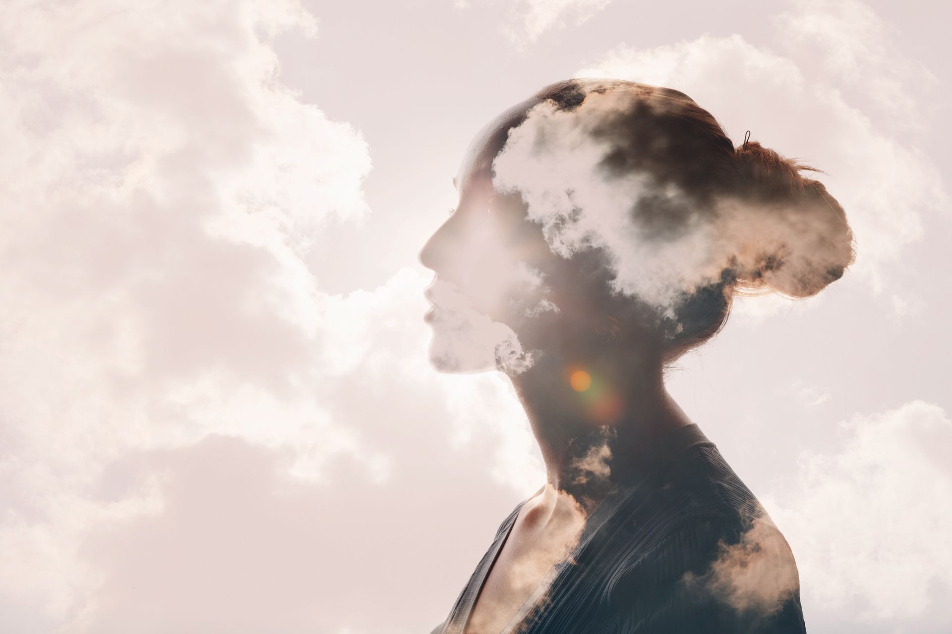 A double exposure of a woman 's face with clouds in her hair.
