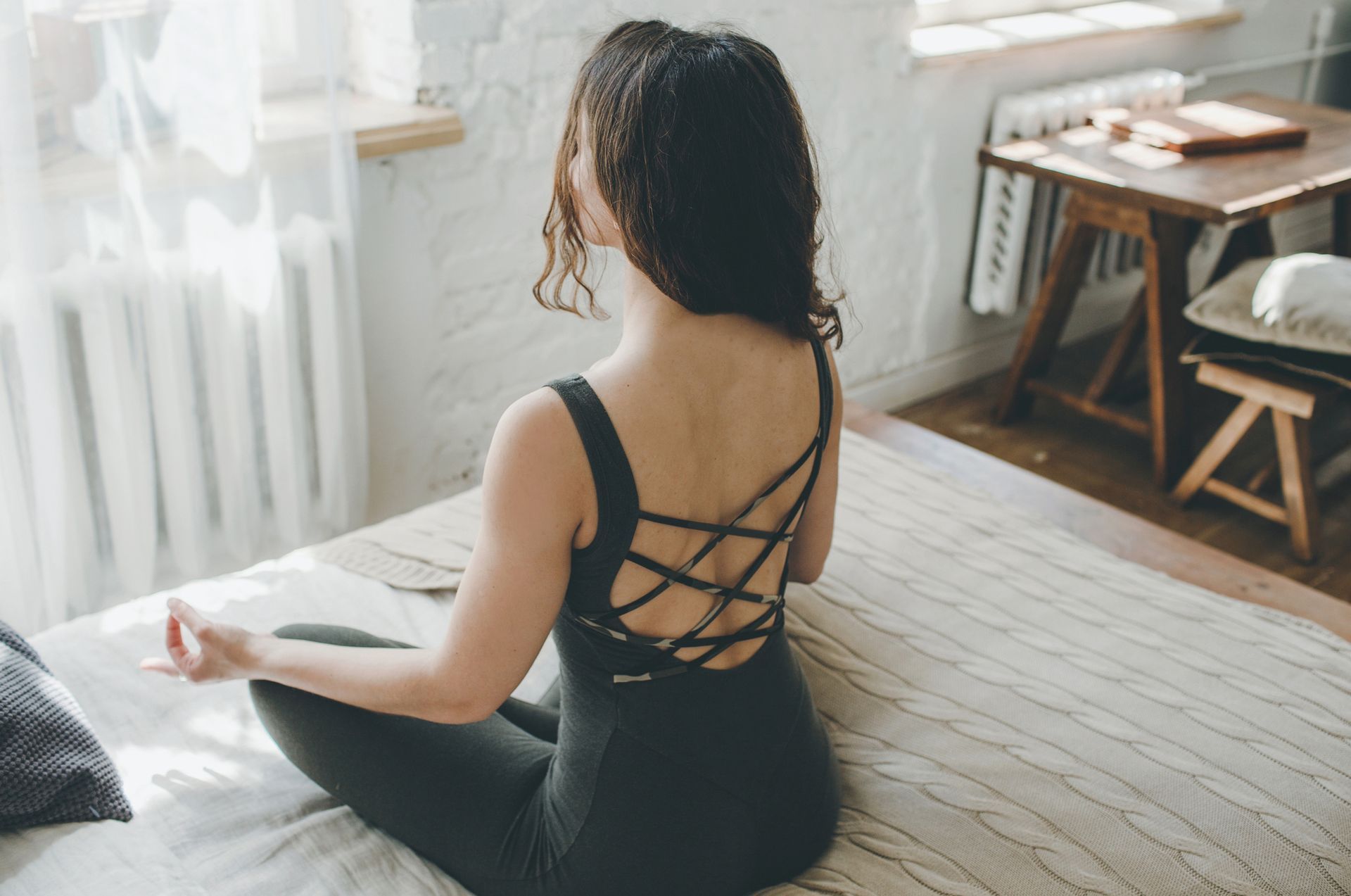 A woman is sitting on a bed in a lotus position.
