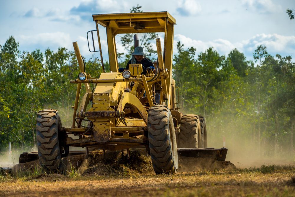 A man is driving a bulldozer through a dirt field.