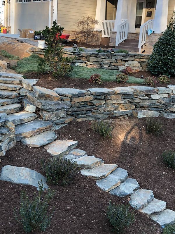 A stone walkway leading to a house with stairs and a stone wall.