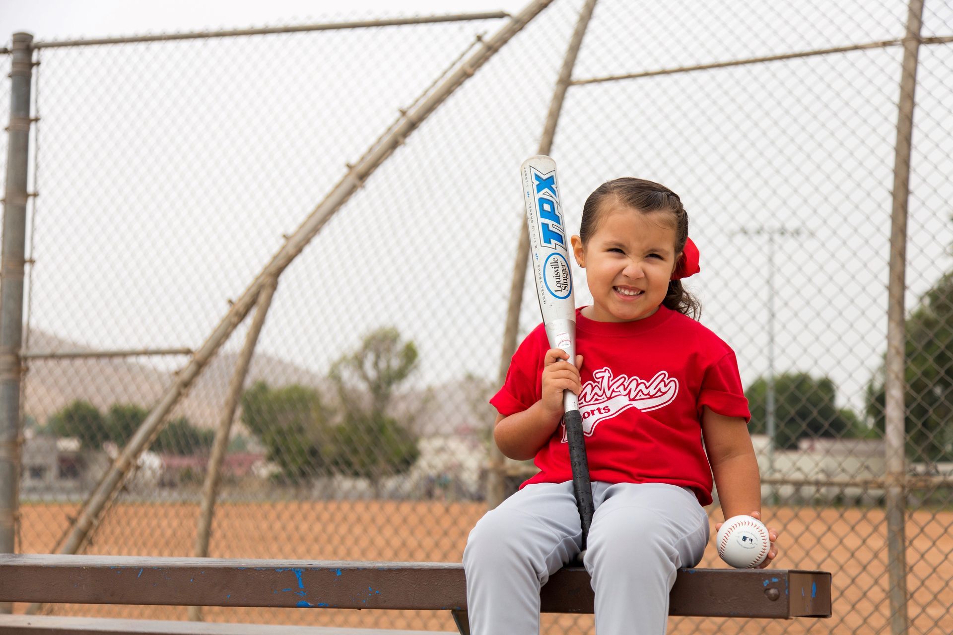 A person wearing a hat and orange shirt, holding a baseball bat on their shoulder on a baseball field.