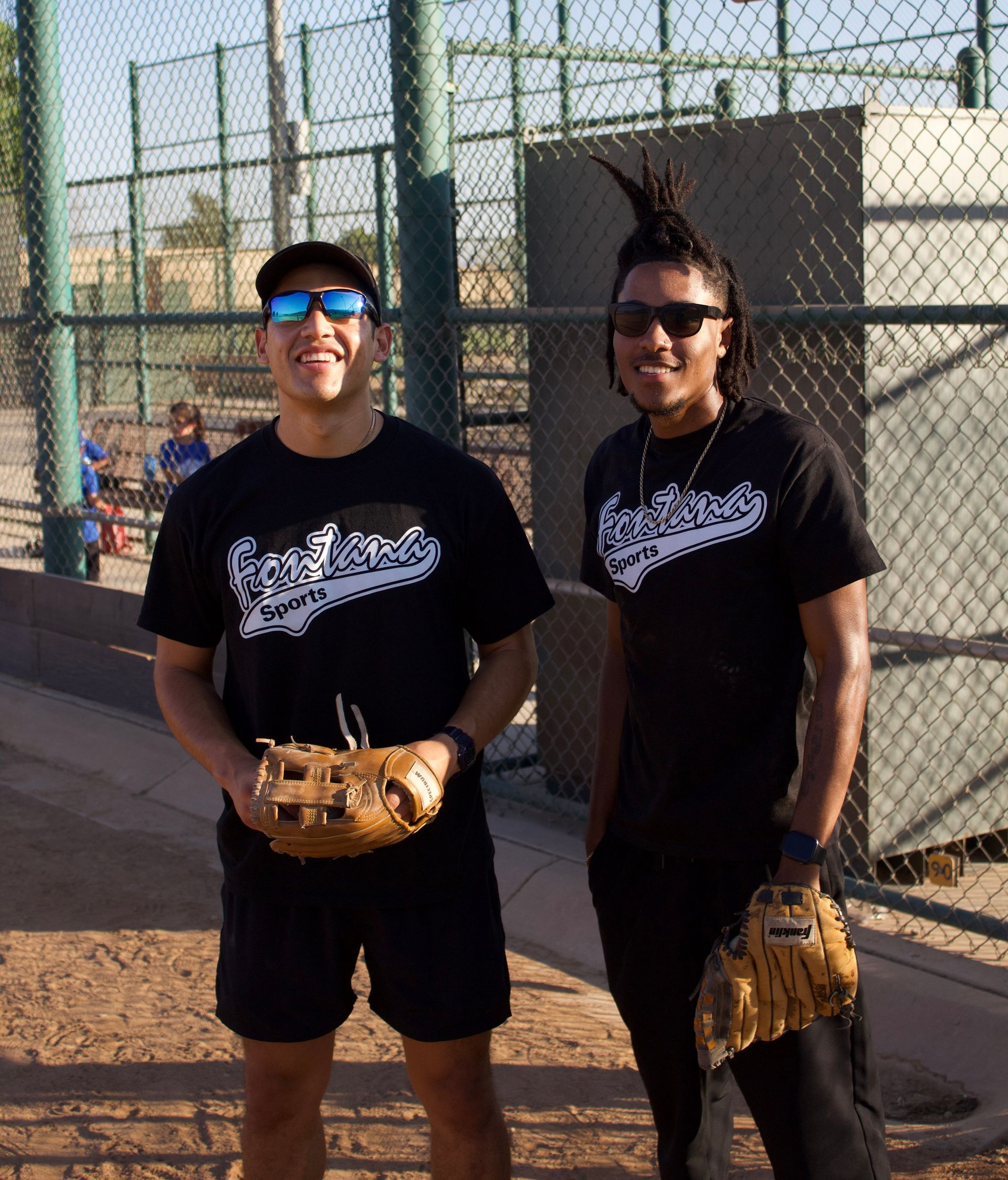 A person wearing a hat and orange shirt, holding a baseball bat on their shoulder on a baseball field.