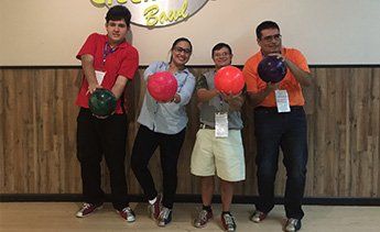 four client holding bowling balls at a bowling alley.
