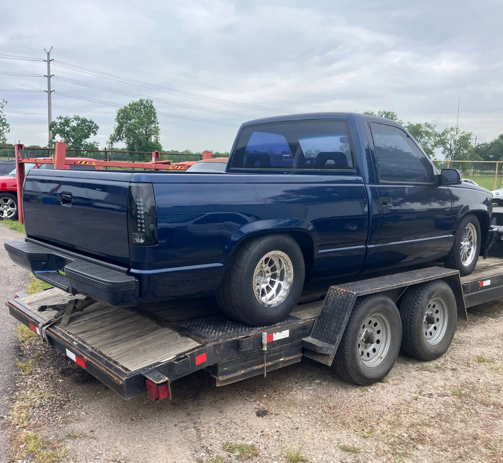Dark blue Chevrolet pickup truck on a black trailer, parked outside. this truck has many performance upgrades and is built for the race track or the road.