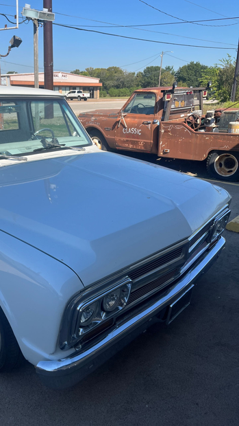 White classic Chevy truck in foreground, rusty tow truck behind it on sunny day.