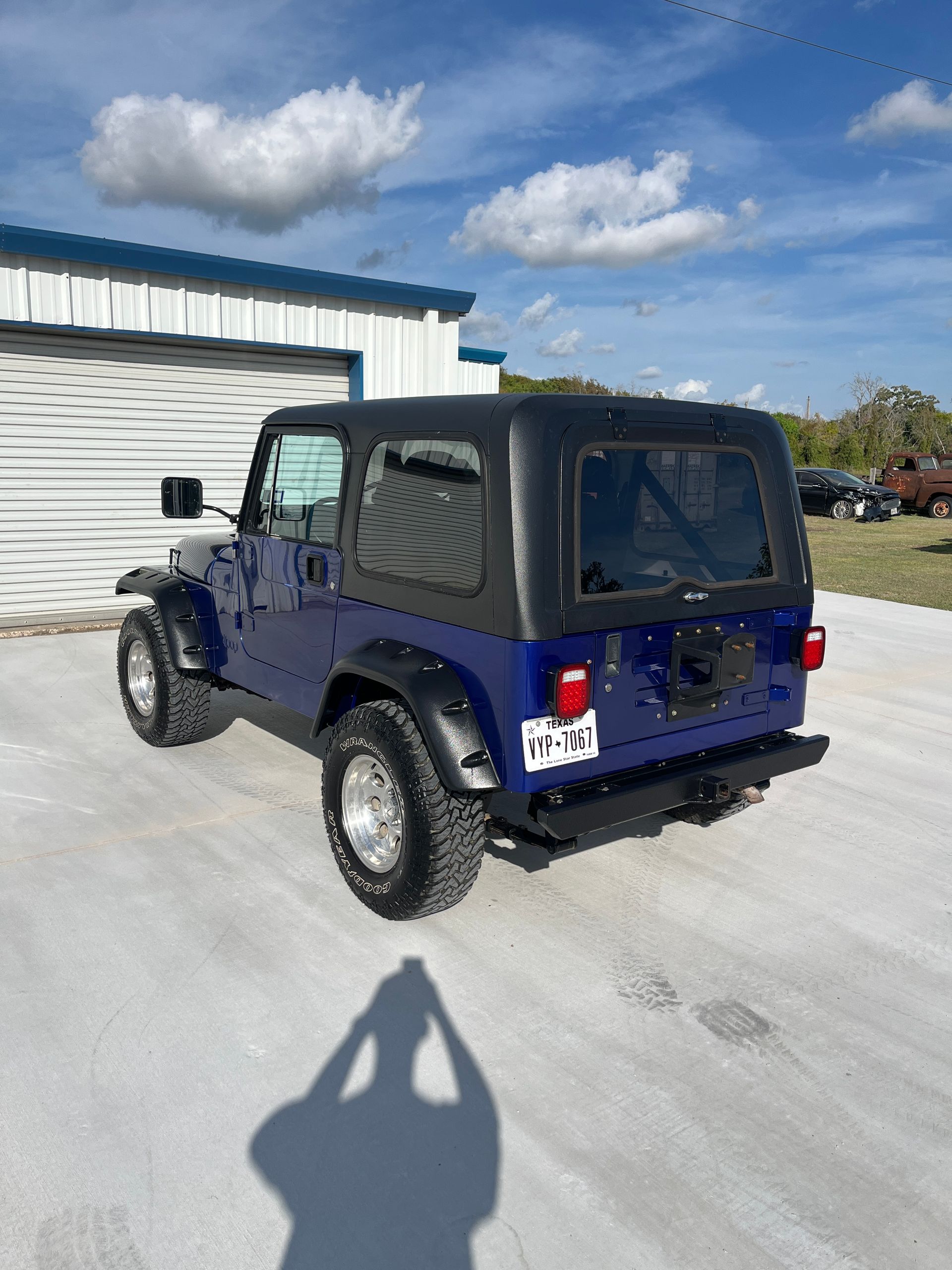 Interior of a tan classic vehicle with a wood steering wheel, dice, and a white shift knob.