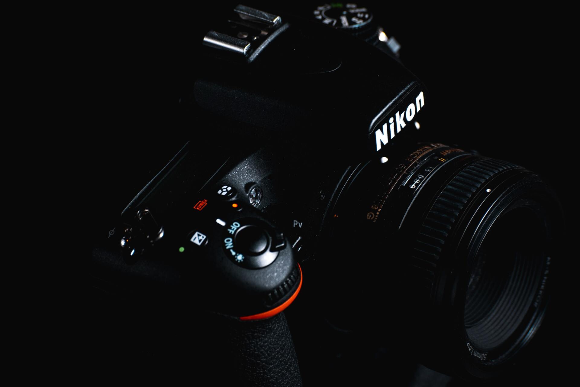 Black Nikon DSLR camera in low light, showing lens and control buttons.