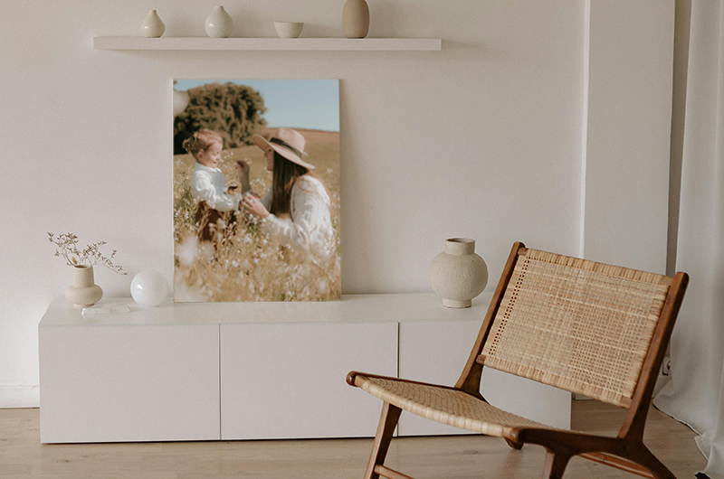 White living room with a photo on a console. A person in a hat holding flowers in a field is visible in the photo. A chair is in the foreground.