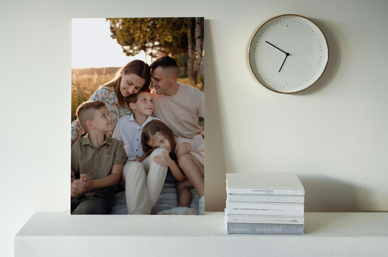 Canvas print of a family portrait on a shelf next to a clock and stack of books.