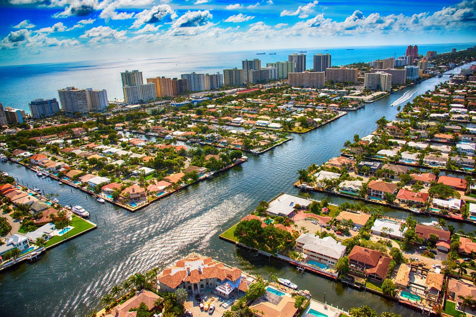 Aerial view of a coastal city with residential homes lining canals, leading to high-rise buildings and the open sea.