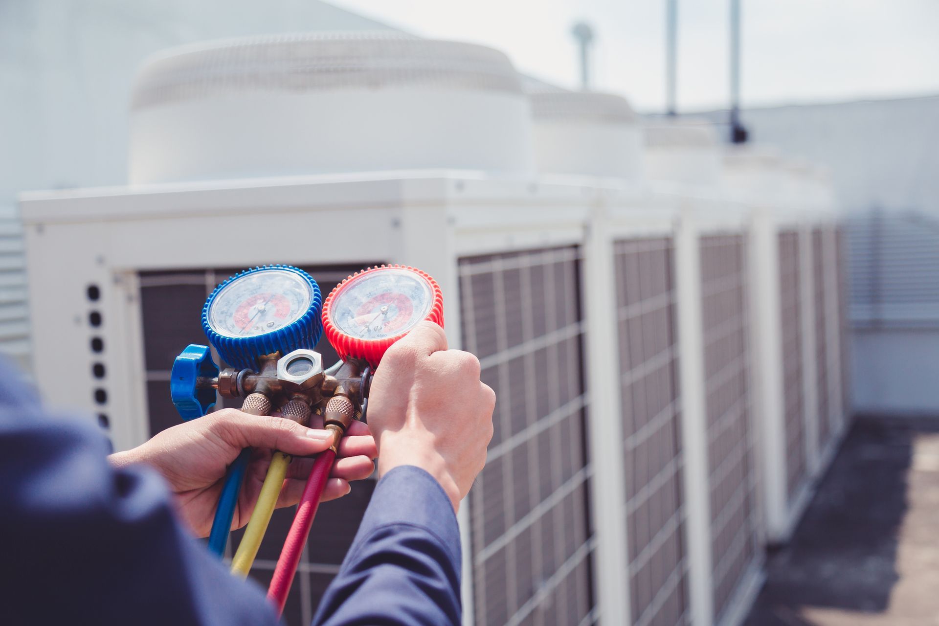 A technician holds a colorful HVAC manifold gauge set while working on rooftop air conditioning units.