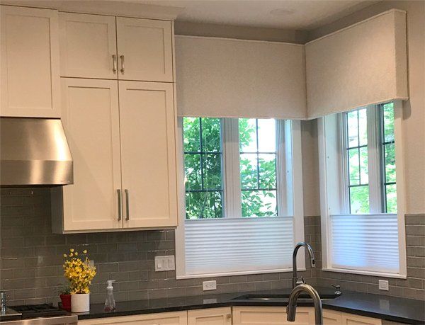 A kitchen with white cabinets , black counter tops , stainless steel appliances and a sink with extra tall valences and bottom up cellular shades