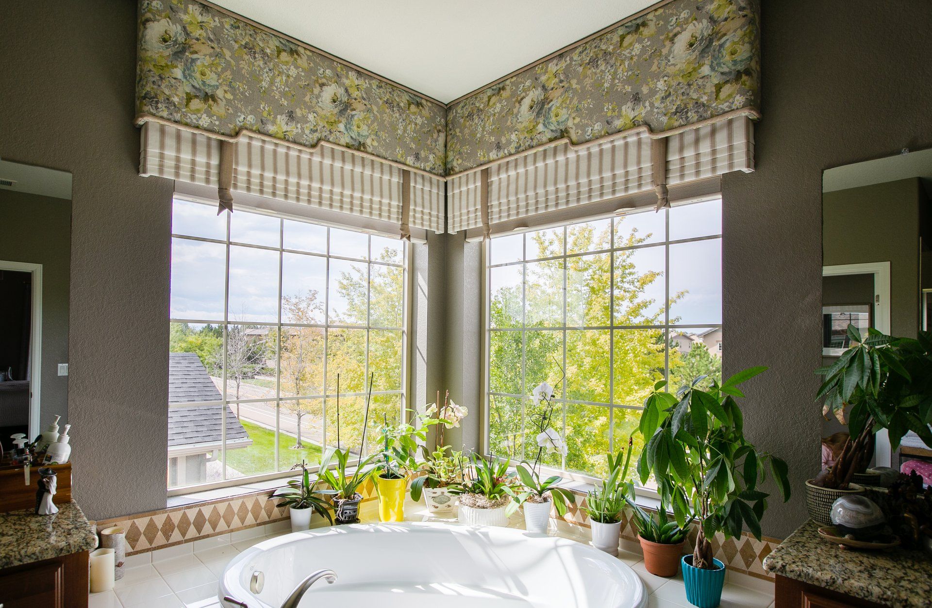 Tub surrounded by plants with striped roman shades and floral cornice