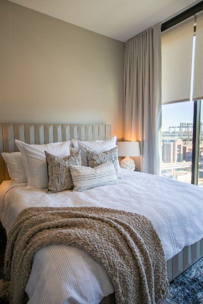 A bedroom with a large bed and a tan linen drapes over a window.