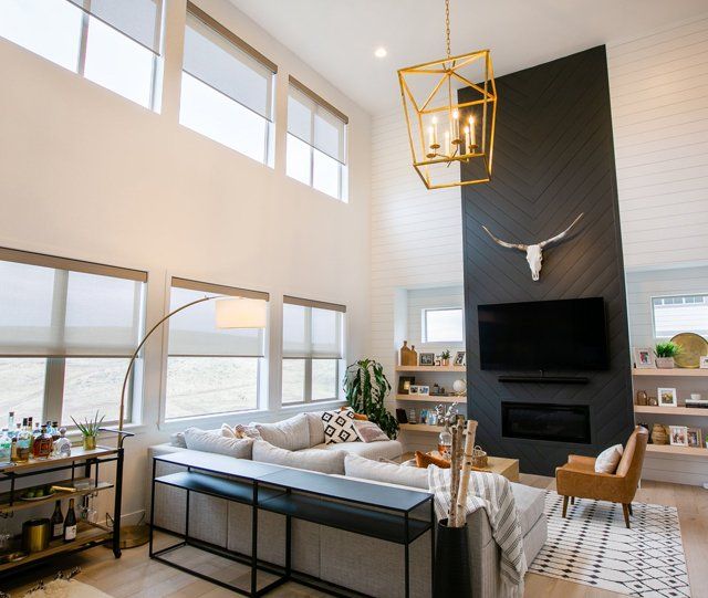 A living room with roller shades on modern windows, a couch , chairs , television and fireplace.