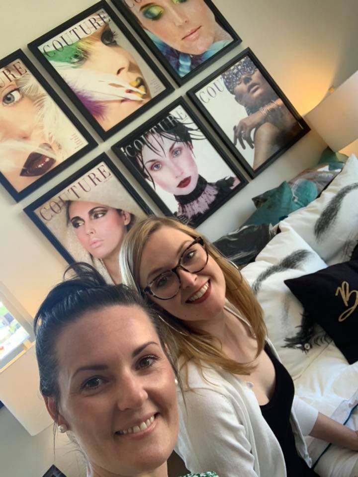 Two women are posing for a picture in front of a wall of couture magazine covers