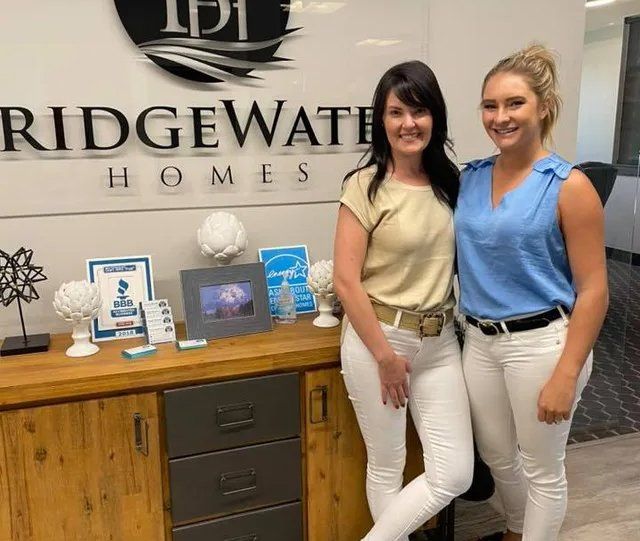 Two women are standing in front of a sign that says ridgewater homes