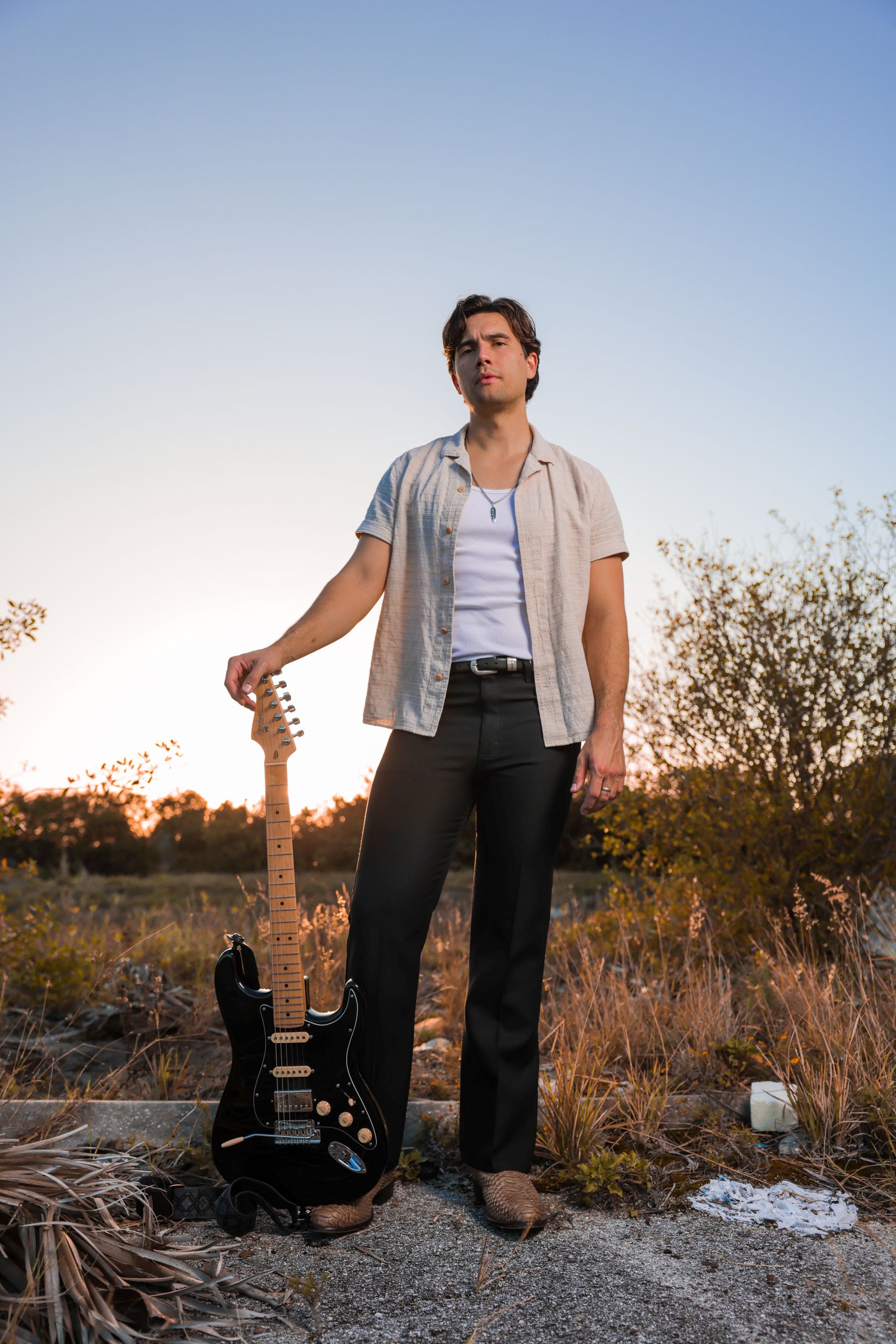 A man is standing in a field holding a guitar.