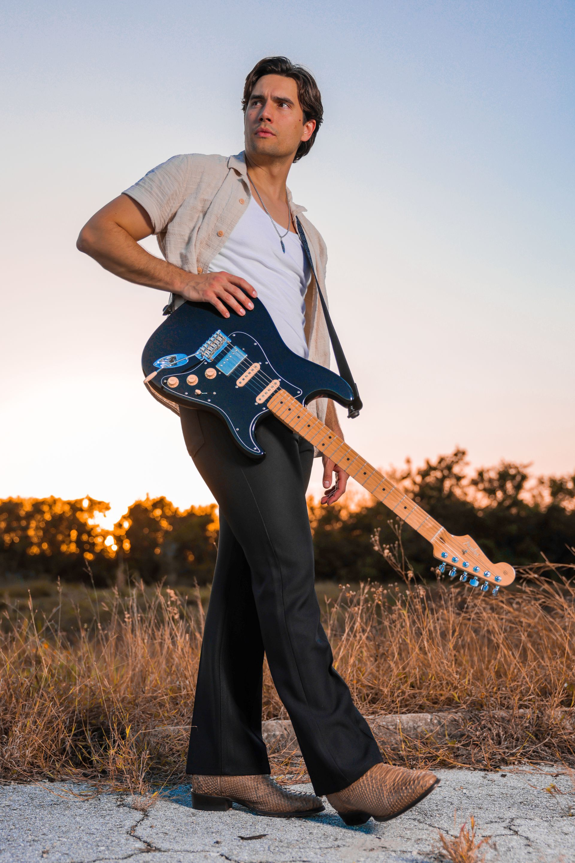 A man is standing in a field holding an electric guitar.