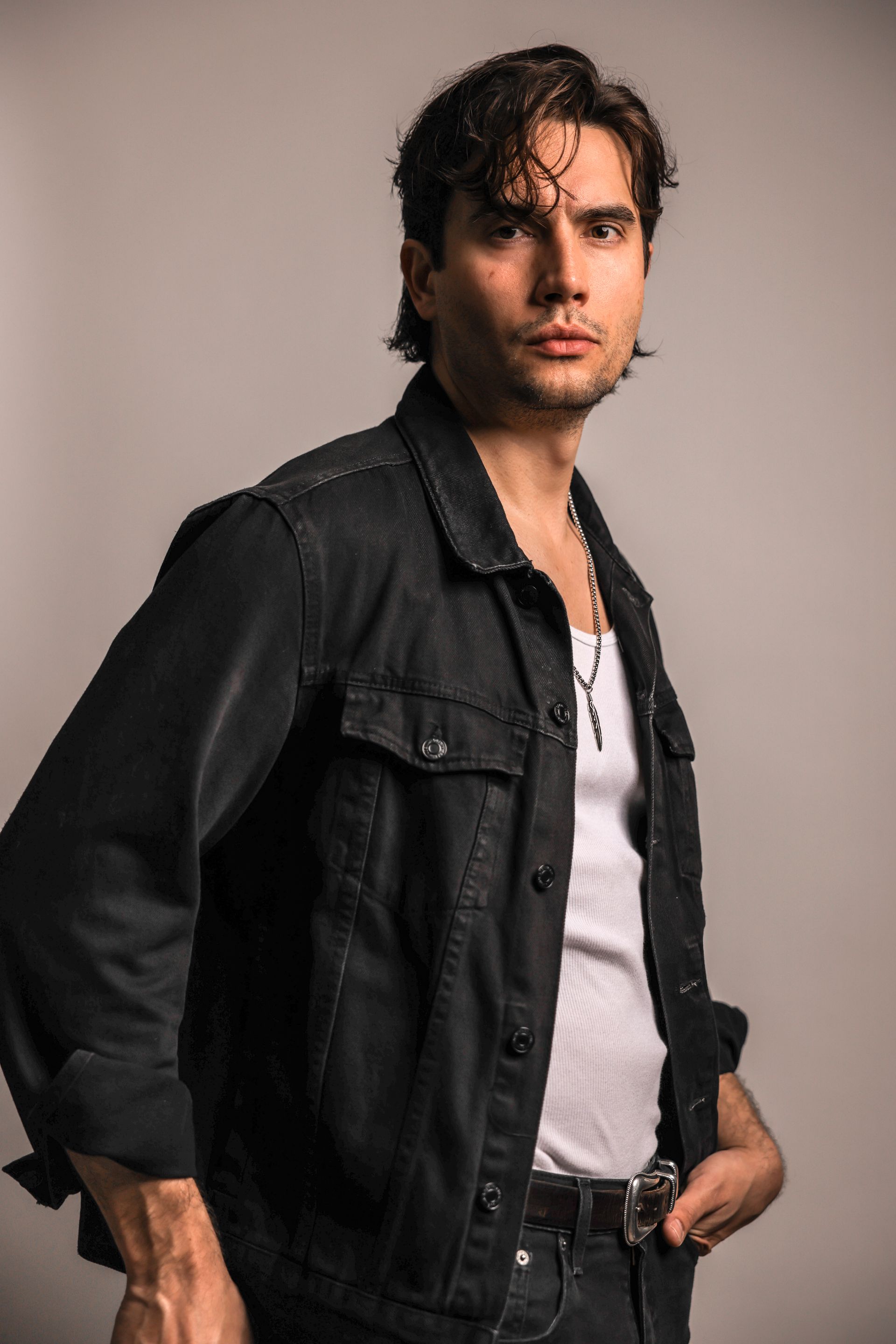 A man wearing a black jacket and a white shirt is standing with his hands in his pockets.