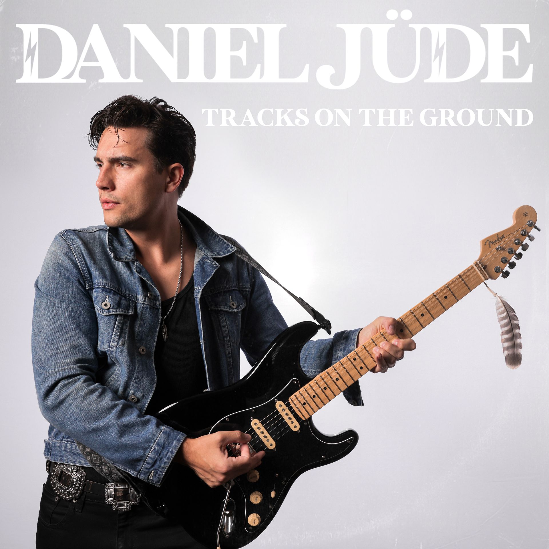 A man in a denim jacket is holding a guitar on the cover of daniel jude tracks on the ground