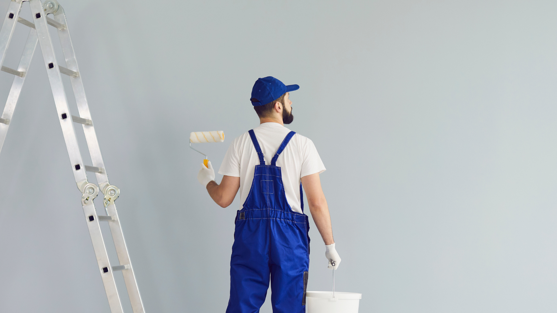 A man is painting a wall with a paint roller and bucket.