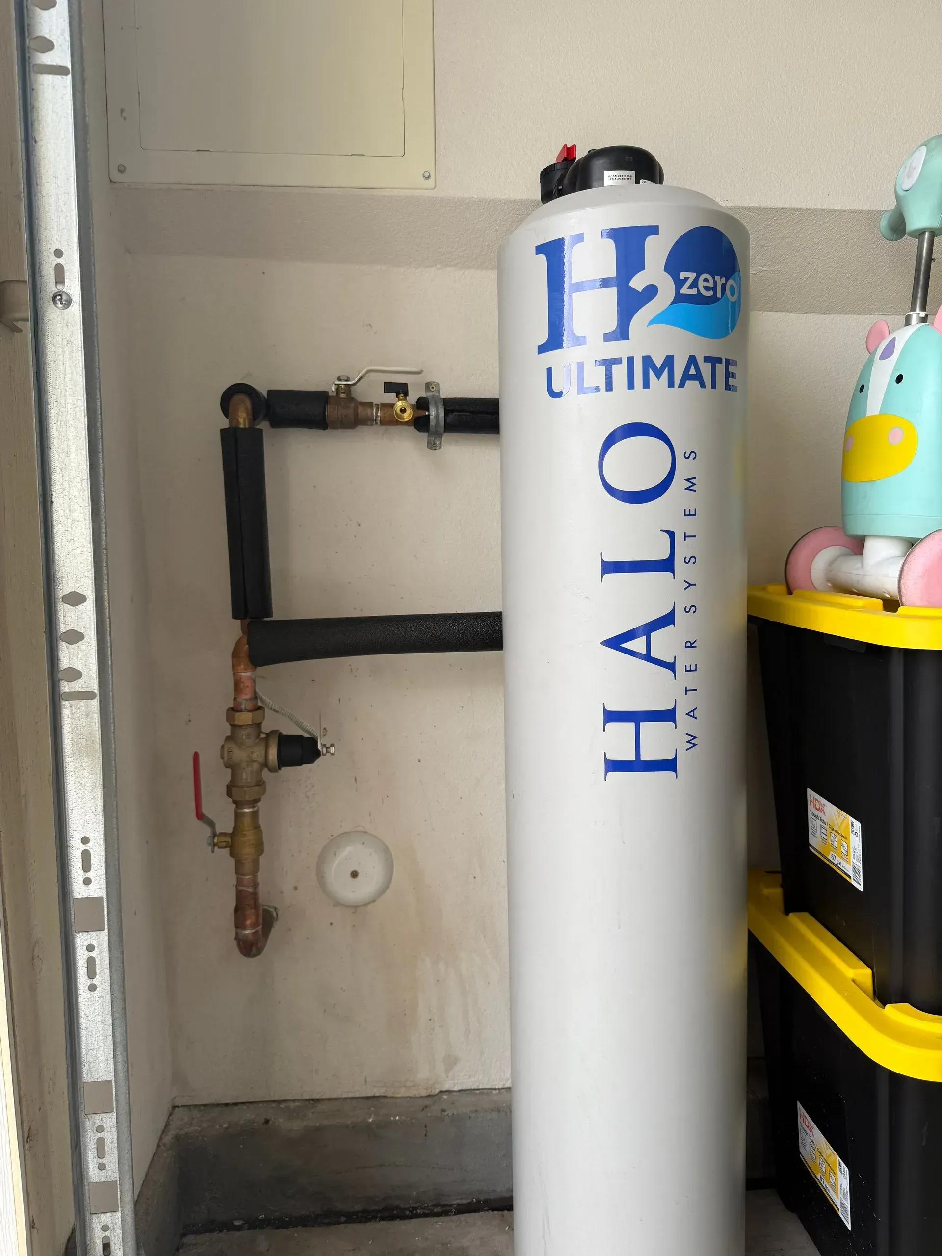 A water filtration system in a utility room. White cylinder with blue text, attached to copper pipes.