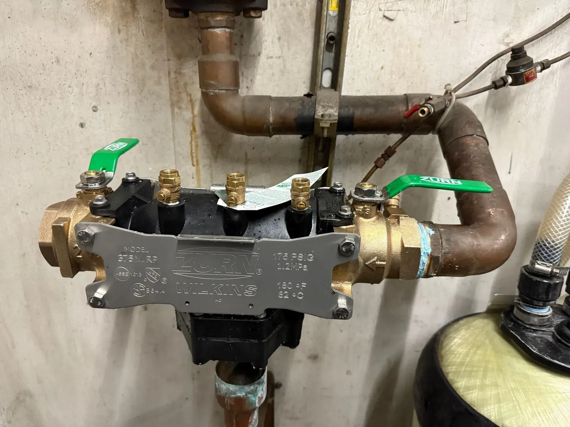 Backflow preventer with green-handled valves and copper pipes, mounted on a wall.