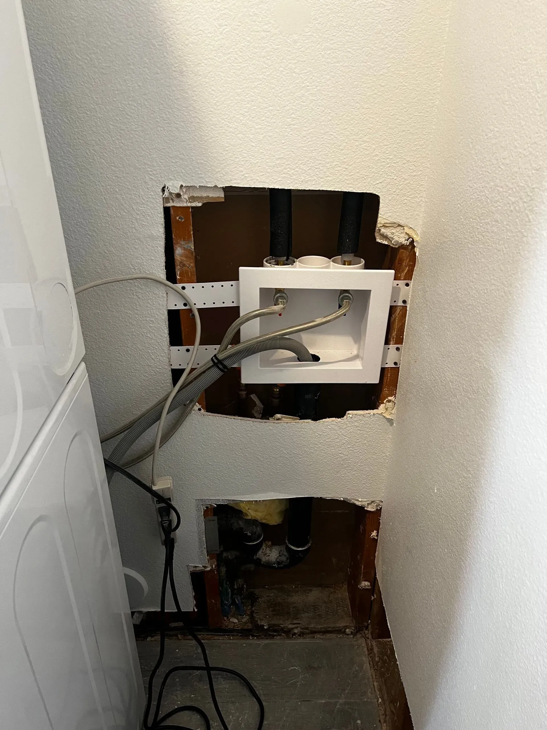 Laundry hookups in a wall with open drywall, showing plumbing and electrical connections.