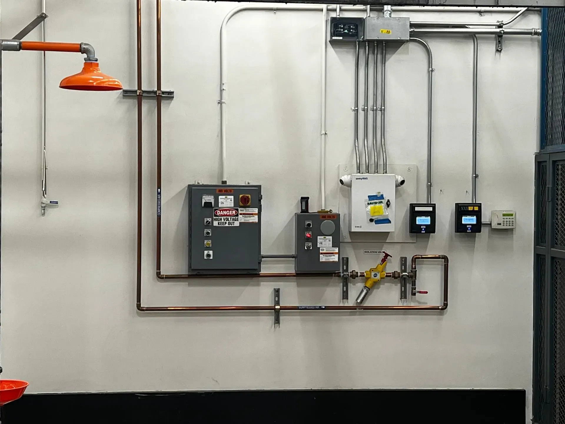 Wall-mounted industrial safety equipment, including an emergency shower, electrical panels, and gauges.