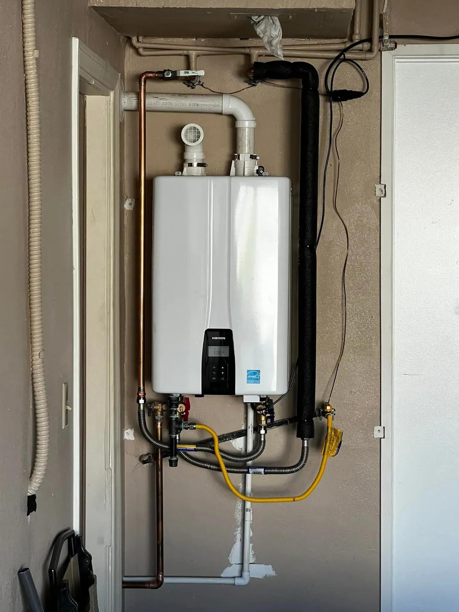 White tankless water heater installed on a wall. Copper and black pipes are connected.