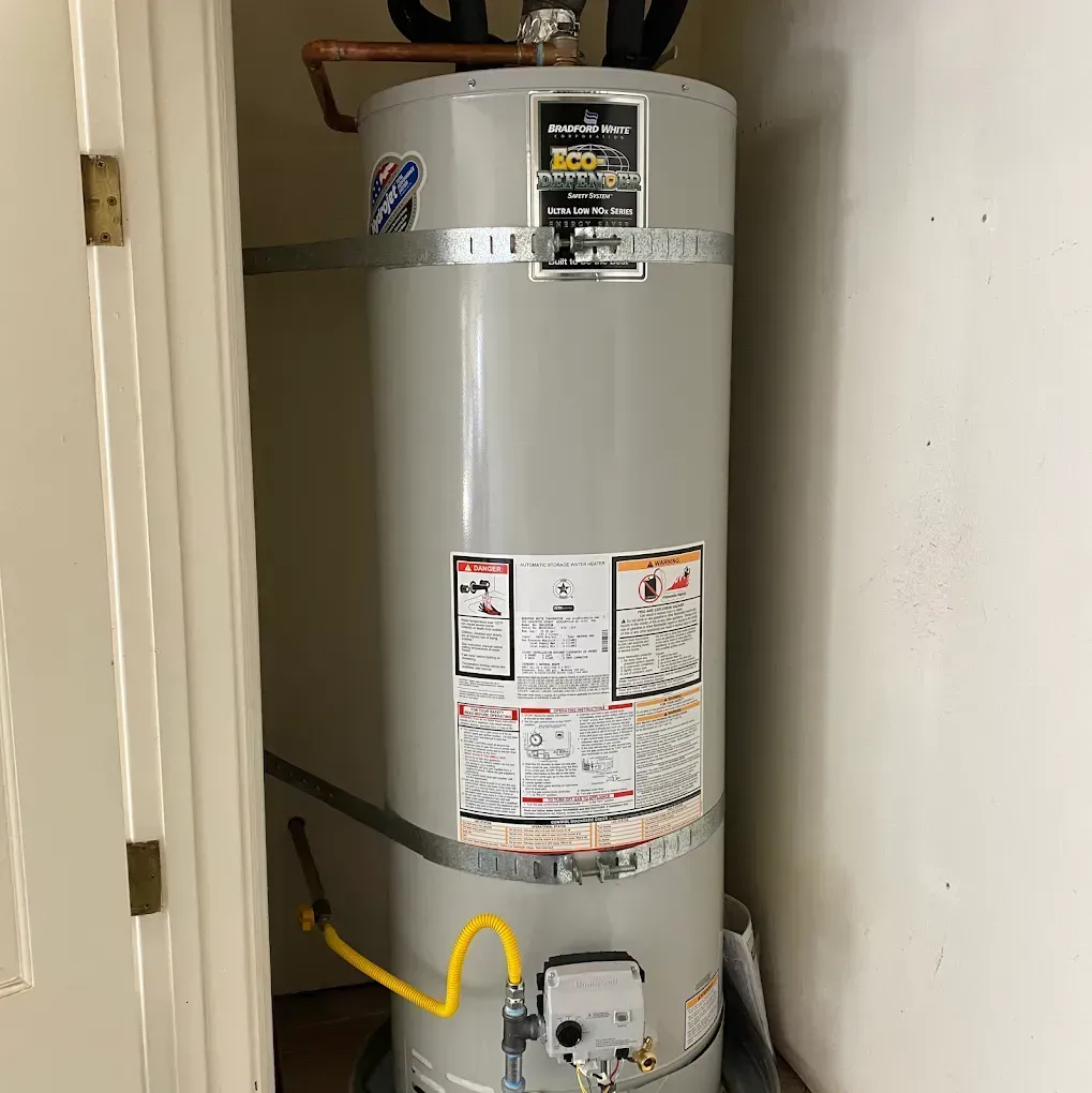 A tall, gray water heater sits in a closet.  Yellow gas line, copper pipes, and warning labels are visible.