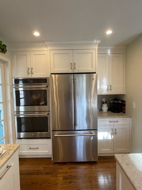 A kitchen wall featuring white cabinetry, a built-in double oven, and a stainless steel French door refrigerator.