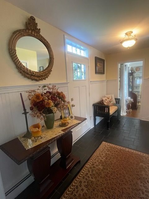 A hallway with a wooden console table, decorative mirror, floral arrangement, and a black bench near a front door.